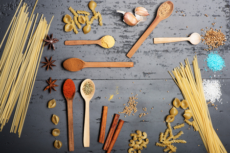 Abstract dry pasta and spices composition made of italian macaroni and asian spices in wooden spoons laid on the grey rough surface, top viewの写真素材