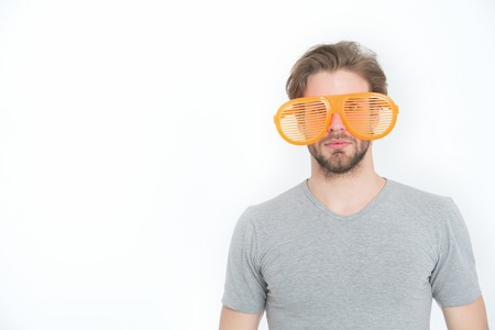young man in grey shirt posing with funny orange big party glasses isolated on white background,...