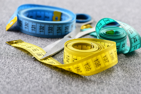 Measuring tapes in different colors rolled and laid on light grey background near metallic scissors, close up and selective focusの写真素材