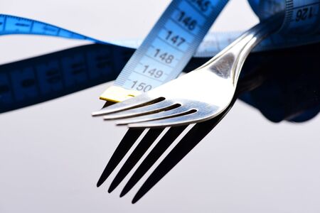 Diet and slim body concept: fork and measuring tape on light grey background with reflection, close upの写真素材