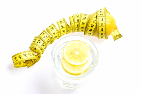 Nutrition and diet concept. Measuring tape twined around lemon with freshly squeezed glass of citrus isolated on white background, copy spaceの写真素材