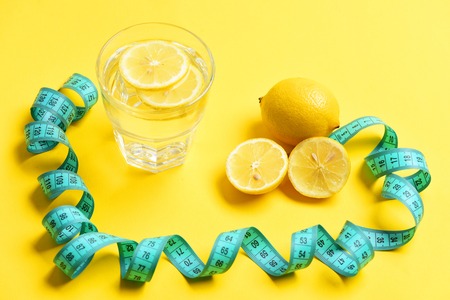 fight against excess weight concept. measuring tape, lemon with freshly squeezed glass of citrus on yellow backgroundの写真素材