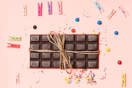 Bar of chocolate tied with vintage thread on pink background and clothespins with drop candies, dragee around, top viewの写真素材