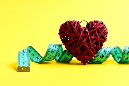 Love fitness and training concept. Measuring tape with red decorative heart on yellow backgroundの写真素材