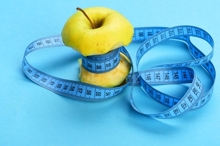 Bitten apple wrapped by blue measure tape spinned around chaotically on light blue background. Diet...