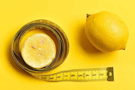 calorie and fitness concept. lemon slice with measuring tape on yellow backgroundの写真素材