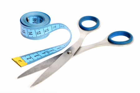 Roll of blue measure tape lying beside silver scissors for tailoring isolated on white background, close up and selective focus. Sewing and creative hobby conceptの写真素材