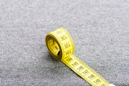Roll of yellow measuring tape with black numbers on it on grey backgroundの写真素材