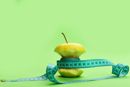 Fruit diet concept: bitten apple wrapped with measure tapeの写真素材