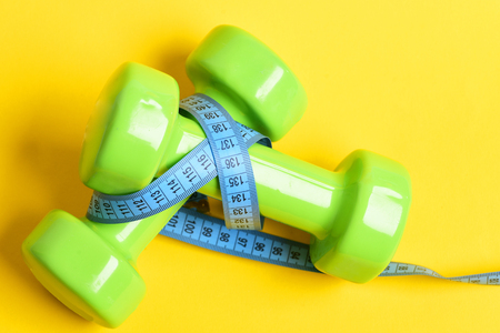 aerobics concept with dumbbells and measuring tape on yellow backgroundの写真素材