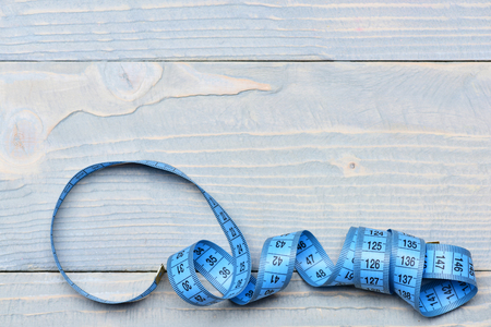 Tape for measuring on vintage wooden background with copy space, top view. Minimalistic concept of tailoring, clothes making and styleの写真素材