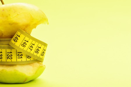Apple and tape for measuring on yellow background as a symbol of health, diet and fitness lifestyle. Close up, copy spaceの写真素材