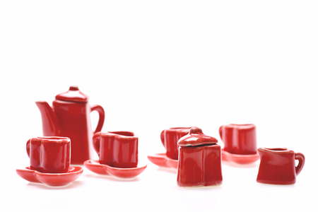 Romantic set of tiny red kitchenware including heart shaped saucers and cups, red ceramic kettle with heart cover, sauce dish and sugar bowl isolated on white background, close up and selective focusの写真素材