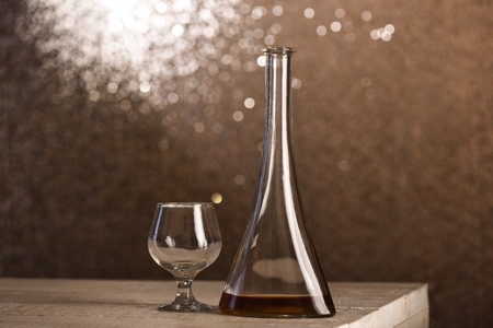 Glass near cone bottle with alcohol beverage on wooden table, on sparkling bokeh silver background, selective focusの写真素材