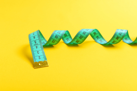 Concept of fitness and slim shape with turquoise twisting measuring tape isolated on yellow...
