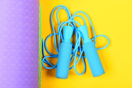Skipping rope in blue colour and purple yoga mat isolated on yellow background, top viewの写真素材