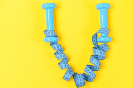 equipment training concept, dumbbells or barbell and measuring tape on yellow backgroundの写真素材