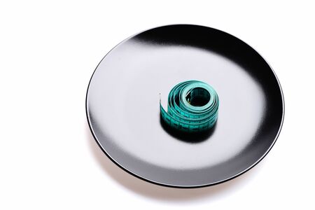 Tape on plate. Roll of cyan blue flexible ruler on black shiny dish isolated on white background....