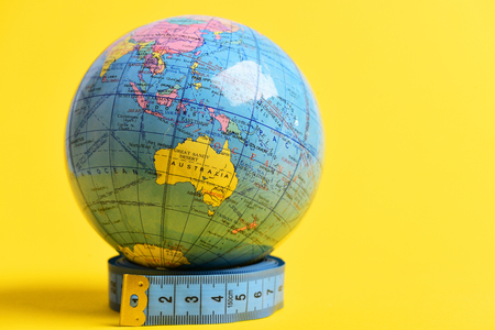 Globe model standing on roll of blue measuring tape isolated on yellow background with copy space. Visible hemisphere which contains Australia on itの写真素材