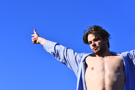 Bearded man, short beard. Caucasian macho with moustache and ruffled hair in blue striped pajamas showing strong chest on torso on blue sunny sky backgroundの写真素材