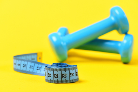 barbell with measuring tape in selective focus on yellow background, fitness object conceptの写真素材
