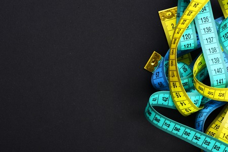 Rulers for sewing in cyan, blue and yellow, twisted on black background with copy space. Concept of diet and weight managementの写真素材