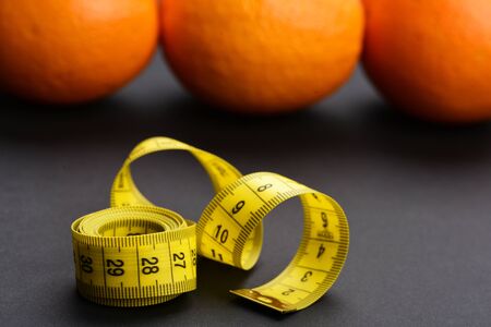 Roll of yellow measuring tape on black surface near oranges. Concept of fruit diet and health nutrition, selective focusの写真素材