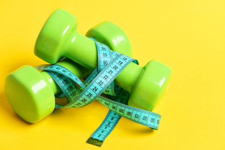 weight loss concept with dumbbells and measuring tape on yellow backgroundの写真素材