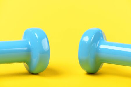Pair of dumbbell tops in light blue color, isolated on bright yellow background. Minimalistic sports conceptの写真素材