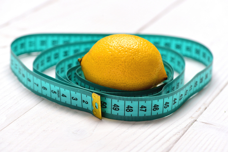 Juicy lemon in middle of cyan measuring tape circles on light wooden background, close up and selective focus. Healthy food and diet conceptの写真素材