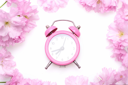 Alarm clock in pink colour and retro style placed in the middle of pink wreath made of sakura flowers isolated on white background, top view. Perfect morning conceptの写真素材