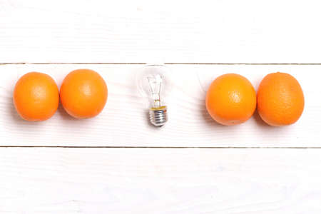 Electric light bulb and oranges in a line on white wooden background, top view and copy space. Healthy food ideaの写真素材