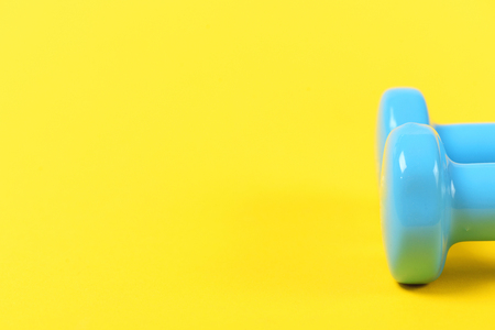 Concept of sports lifestyle and athletics: tops of blue lightweight dumbbells isolated on yellow background with copy spaceの写真素材