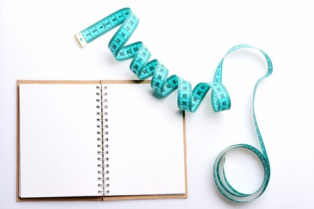 Notebook with open blank pages on binder and twisted cyan blue measuring tape isolated on white background, copy space and top view. Diet notes and regime conceptの写真素材