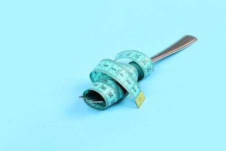 Fork of metal wrapped around with cyan tape for measuring, isolated on light blue background. Concept of diet, weight loss and healthy nutritionの写真素材