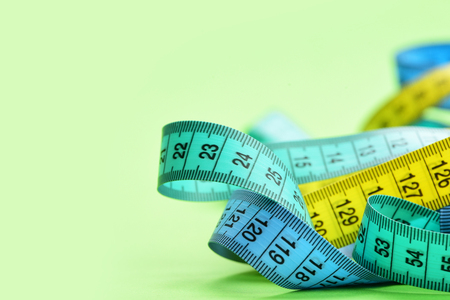 Measure tapes in cyan, blue and yellow colors twisted disorderly, isolated on light green background with copy space, close up and selective focusの写真素材