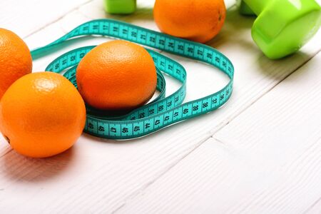 Oranges lying in circles of cyan measuring tape on white wooden surface and green dumbbells on background, close up and copy space, selective focus. Concept of healthy food for fit shapeの写真素材