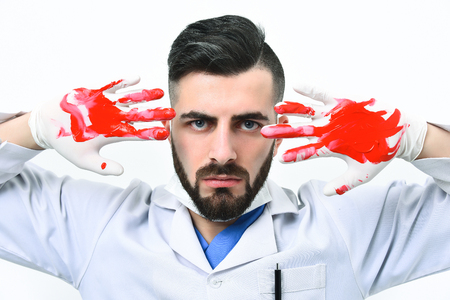Doctor with angry face expression and dark beard shows blood on his gloves, isolated on white backgroundの写真素材