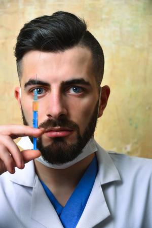 Concept of medical profession: bearded doctor with serious face expression and syringe with drug in hand on beige backgroundの写真素材
