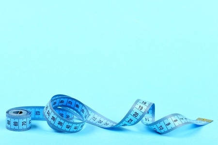 Tape for measuring in blue color untwisted on turquoise background with copy space
