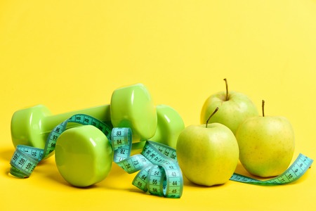 Dumbbells and apples composition: apple fruit, sport units and long turquoise measuring tape isolated on striking yellow background. Concept of sport regime, strong diet and healthの写真素材