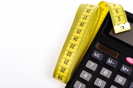 Calculate your diet. Plastic calculator with folded yellow sewing centimeter isolated on white background. Concept of dieting and measurementの写真素材