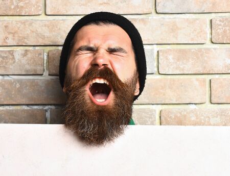 Bearded man, long beard. Brutal caucasian shouting unshaven hipster in black hat with white paper...