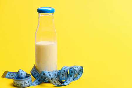 Bottle of white milk and measuring tape in blue color isolated on yellow background, copy space. Concept of size, healthy nourishment and fit bodyの写真素材