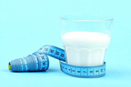 Tape for measuring ties around glass of milk, isolated on light blue background. Concept of vitamin diet and calcium nutritionの写真素材