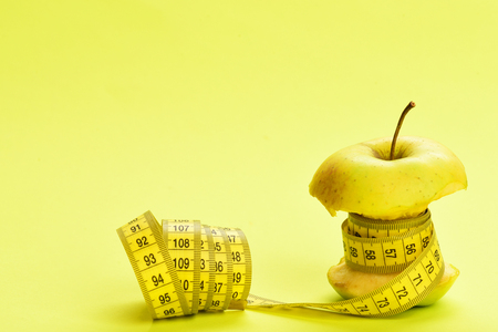 Concept of healthy lifestyle and weight management: apple wrapped by measuring on yellow background with copy spaceの写真素材
