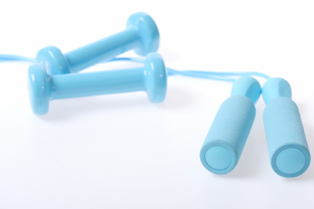 Pairs of skipping rope handles and cyan blue dumbbells defocused and isolated on white background, copy space. Concept of body fitnessの写真素材