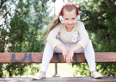Cute little girl enjoying music using headphones at summer day