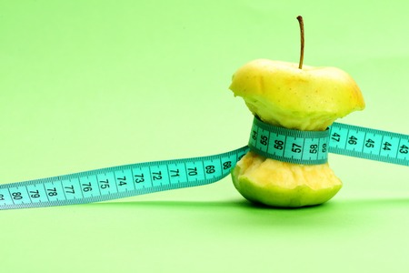 Concept of healthy nutrition, fruit diet and eco food: cyan tape for measuring ties around bitten apple on light green background with copy spaceの写真素材