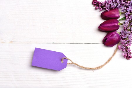 Flowers with card. Wood background in white colour with purple bunch of tulips and lilac tied to violet note tag, copy space and top view. Spring surprise conceptの写真素材